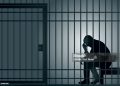 Concept of prison and arrest of an offender or criminal, with a prisoner sitting in his cell holding his head in his hands.