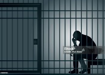 Concept of prison and arrest of an offender or criminal, with a prisoner sitting in his cell holding his head in his hands.
